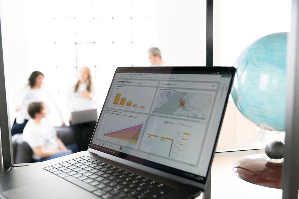 Aufgeklappter Laptop mit einem Dashboard aus Balkendiagrammen und einer Kartenansicht, dahinter das Team im Unschärfebereich